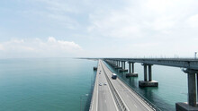Summer View From A Helicopter. Action. A Huge Bridge For Moving Cars Made High Above The Sea And The Blue Daytime Sky.
