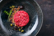 Modern style gourmet tartar raw from beef filet with capers and amarena cherry served with truffle cream and lettuce as top view in a Nordic design plate with copy space right