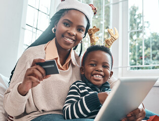 Wall Mural - Were doing some Christmas shopping from home. Shot of a woman holding her credit card and holding a digital tablet while sitting with her son during Christmas time.