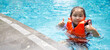 © chadchai - Asian child playing in the pool. Wearing orange life jacket, smiling with thumbs up.