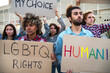 © Daniel - Multiracial group of people march together protesting on a demonstration for LGBT rights holding cardboard banners.