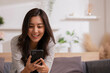 © sopradit - At home, an Asian woman waving a smartphone app enjoys online virtual video chat with pals in a virtual meeting while sharing stories for social media.