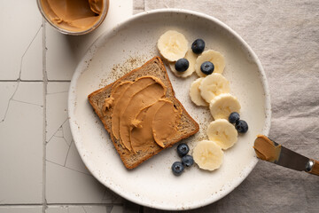 Sticker - Peanut butter toast with banana slices on ceramic plate. Healthy breakfast or snack on white tile background, top view