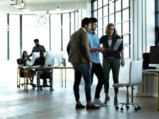 Canvas Print - Ive got something to show you guys. Full length shot of three business colleagues looking at something on a laptop in their office.