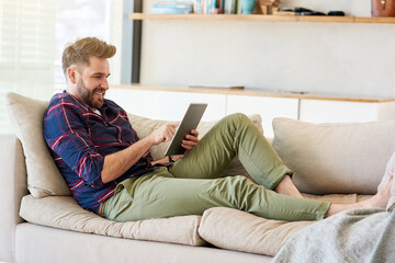 Poster - Chilled vibes online. Shot of a relaxed young man using a digital tablet on the sofa at home.