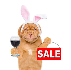 Poster - Smiling puppy wearing easter rabbits ears holds sales symbol and  glass of red wine. Isolated on white background