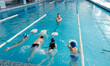 A group of boys and girls train and learn to swim in a modern swimming pool with an instructor. Development of children's sports. Healthy parenting and promotion of children's sports.
