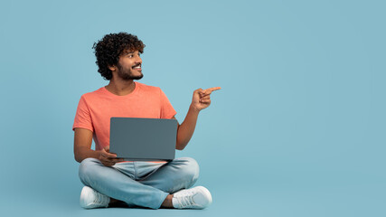 Handsome indian man using modern laptop on blue, copy space