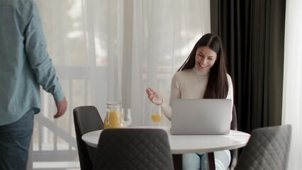 Wall Mural - Young couple using laptop computer on the table in the living room and drinking orange juice