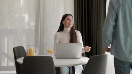 Wall Mural - Young couple using laptop computer on the table in the living room and drinking orange juice