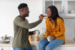 © Prostock-studio - Cheerful Young Black Couple Eating Snacks In Cozy Kitchen Together