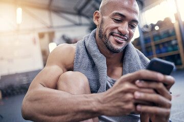 Wall Mural - This app is amazing for tracking my results. Shot of a muscular young man using a cellphone while taking a break from exercising in a gym.