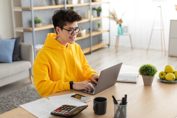 Smiling asian man working on laptop at home