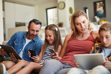 Sticker - The future of family time is now. Shot of a happy young family using wireless devices on the sofa at home.