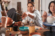 © Yakobchuk Olena - Woman giving brush to her friend while glazing clay pots at the master class