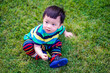 © suppa - Kid sit thoughtful on the grass with idea space. Cute baby boy in a striped colorful t shirt sit and play in the garden on a Sunny summer day. Little child sit and playing dry leaves in the park.