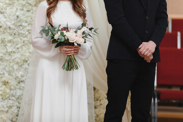 Wall Mural - wedding day. bride in long white dress with bouquet of flowers and groom in black suit on wedding ceremony