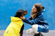 Low angle view of woman and dog with yellow raincoat. Horizontal view of woman caressing rottweiler under the rain isolated on blue background. People and animals concept.
