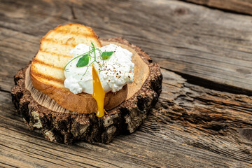 Wall Mural - Close up poached egg with liquid yolk with fresh leaves on toast on brown rustic wooden background. English muffin. egg on toasted bread for healthy breakfast or snack. place for text, top view