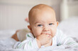 baby 4 months old holds fingers in his mouth, portrait of cute baby on the bed
