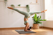 © 220 Selfmade studio - Side view Asian woman wearing green sportwear doing Yoga exercise in front windows,Yoga Forearm Stand pose or Pincha Mayurasana,Calm of healthy young woman breathing and meditation yoga at cozy home