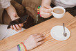 © illustrissima - Lesbian couple drinking coffee in a cafe and serfing in smartphone close up. Hands holding rainbow hearts