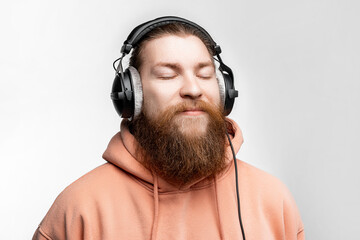 Wall Mural - Scandinavian handsome contented man closed his eyes and listens to music in professional headphones isolated on gray background. Happy guy with ginger hairstyle and beard. Modern digital technologies