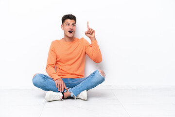 Young man sitting on the floor isolated on white background intending to realizes the solution while lifting a finger up