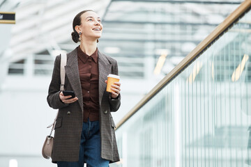 Waist up portrait of smiling young businesswoman walking towards camera in office building while starting work in morning, copy space