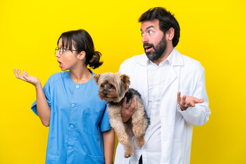 Wall Mural - Young veterinarian couple with dog isolated on yellow background with surprise facial expression