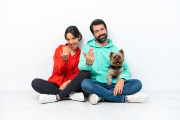 Poster - Young caucasian couple sitting on the floor with their pet isolated on white background inviting to come with hand