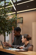 © Seventyfour - Vertical warm toned portrait of two young colleagues discussing work at standing desk in modern office