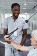 © Seventyfour - Vertical portrait of smiling rehabilitation therapist assisting senior man at gym in clinic