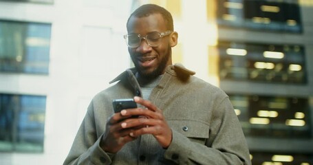 African-American man uses a mobile phone standing near a building in Evening