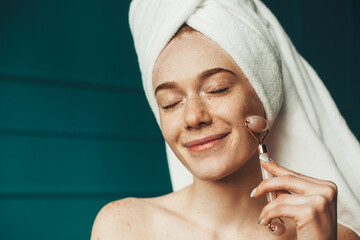 Smiling woman with eyes closed using jade facial roller for skin care. Beautiful portrait. Natural stone. Beauty skin female face.