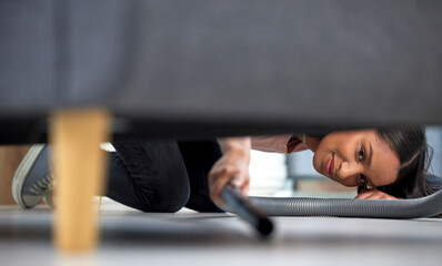 Poster - For every minute spent on cleaning, an hour is earned. Shot of a young woman vacuuming under the couch at home.