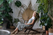 © DimaBerlin - Health and well-being benefits of plants. Young happy dreamy italian woman in dress relaxing in tropical resort-style garden at home, relaxed spanish female gardener resting after work in greenhouse