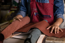 Tanner Woman Selective Leather Goods On Workshop, Selected Pieces Of Beautifully Colored Or Tanned Leather On Leather Craftman Work Desk, Working Process Of Leather Craftsman.