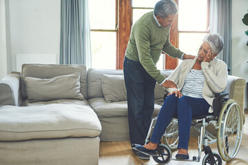 Sticker - We will get through this together. Shot of a worried looking elderly woman seated in a wheelchair while being supported and held by her husband inside at home during the day.