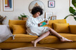 © Daniel - African american woman relaxing at home reading a book sitting on couch.