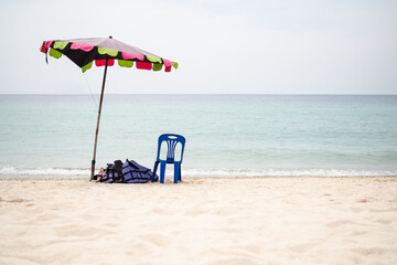 Parasol Umbrella, life jacket, plastic chair on Sand Beach at Coast with Blue Sea and Blue Sky. for Tourism Relax Vacation Travel Tropical Summer Holidays Nature Water Ocean Island conept.