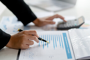 Wall Mural - Business woman hand pointing to a financial data graph and presses the calculator to calculate the income budget.