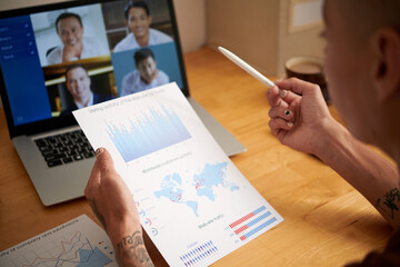 Wall Mural - Marketing department manager holding report with charts showing customers activity when talking to colleagues in online meeting