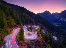 The Mountain Pass Of Maloja, Switzerland. A Road With Many Curves Among The Forest. A Blur Of Car Lights. Landscape In Evening Time. Large Resolution Photo For Travel