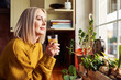© baranq - Mature woman drinking glass of water in the kitchen looking through the window