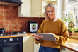 © baranq - Mature woman using digital tablet at home in a kitchen