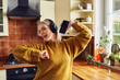 © baranq - Joyful mature woman dancing in kitchen while listening music on headphones