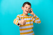 © luismolinero - Little boy isolated on blue background keeping a conversation with the mobile while doing thumbs up