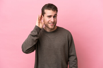 Wall Mural - Young caucasian man isolated on pink background listening to something by putting hand on the ear