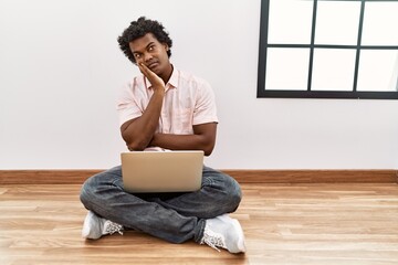 Canvas Print - African man with curly hair using laptop sitting on the floor thinking looking tired and bored with depression problems with crossed arms.